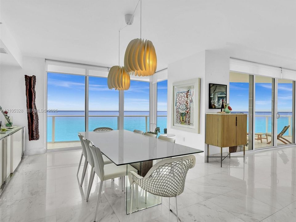 Elegant dining area featuring floor-to-ceiling glass doors and windows, large-format tile flooring, contemporary pendant lighting, and a glass-top dining table.
