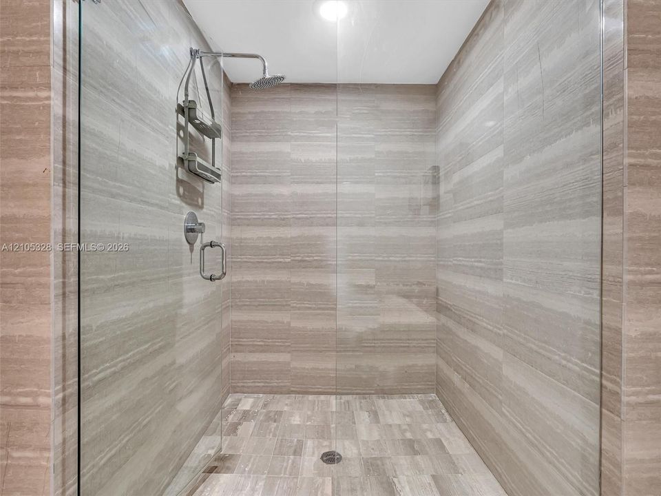 Luxurious spa-inspired shower featuring a frameless glass enclosure, ceiling-mounted rainfall showerhead, handheld shower, and elegant horizontally patterned wall tiles.
