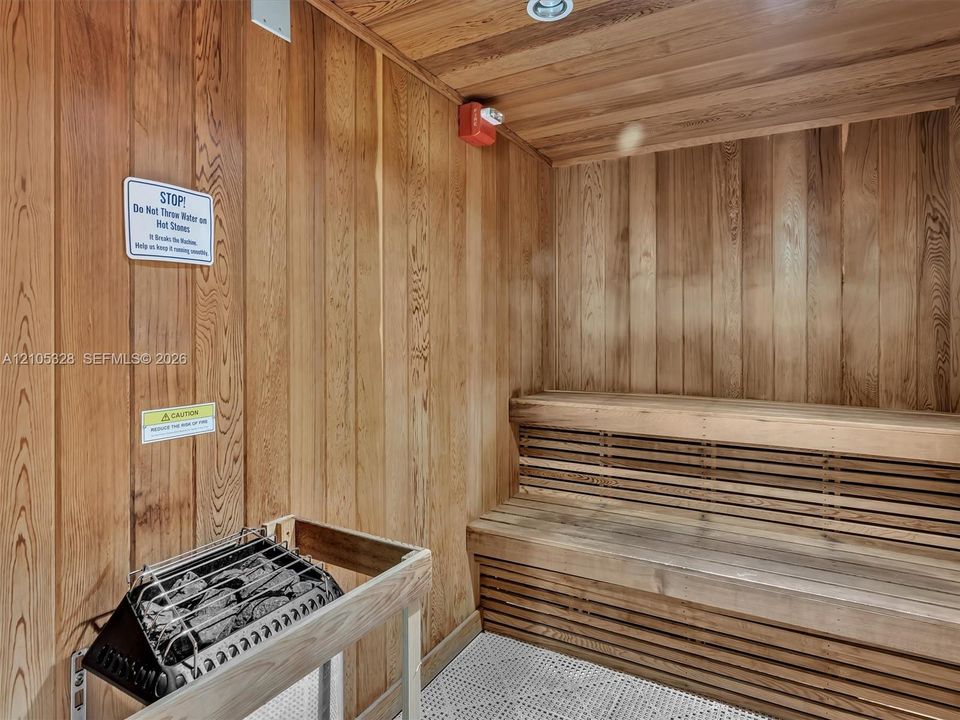 Wood-paneled sauna featuring built-in wood benches, a sauna heater with protective railing, and recessed ceiling lighting