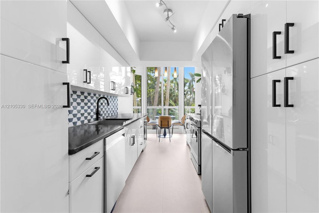 Galley kitchen featuring white cabinetry, black countertops, a geometric tile backsplash, stainless steel appliances, and track lighting