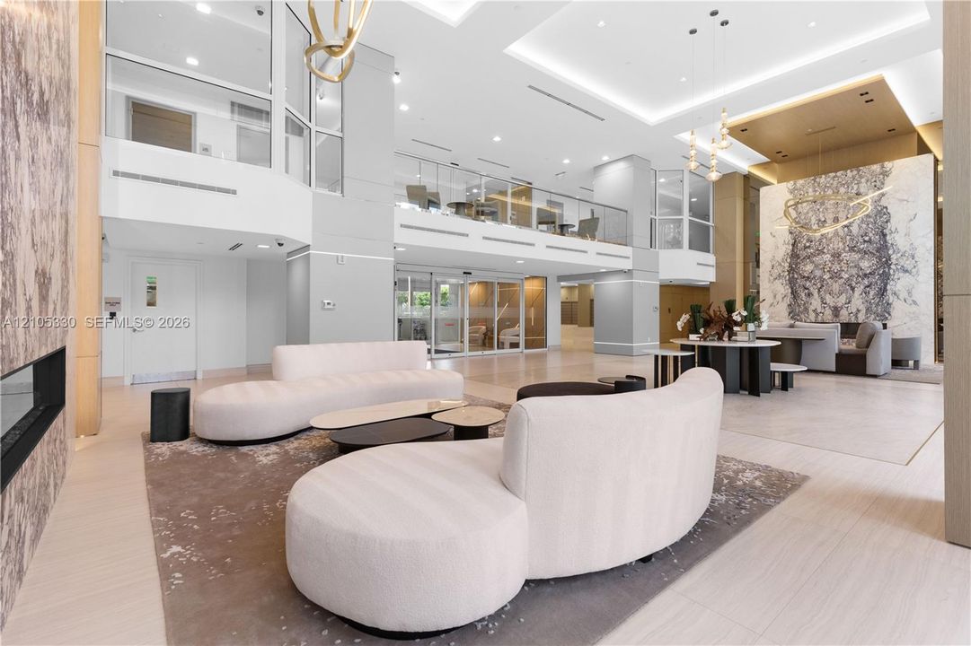 Two-story lobby with high ceilings, recessed lighting, a built-in fireplace, and a glass-paneled mezzanine