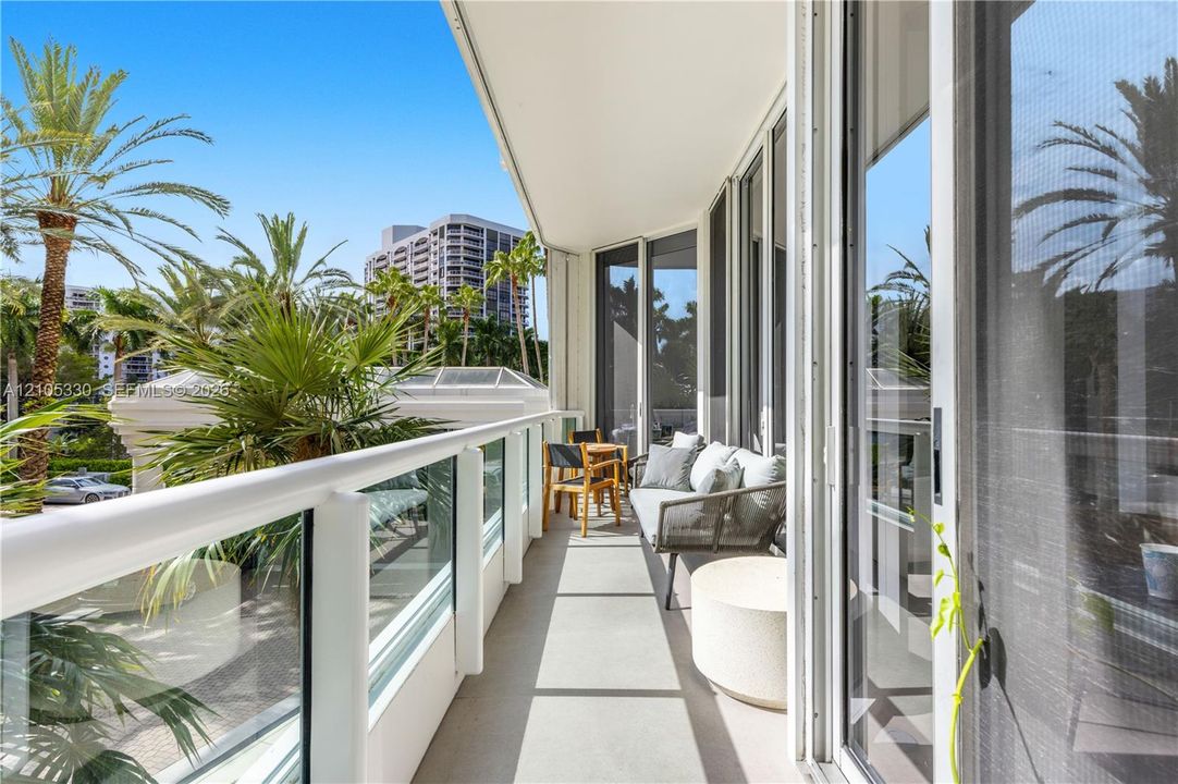 Expansive balcony featuring a glass and white railing, concrete flooring, and full-height sliding glass doors