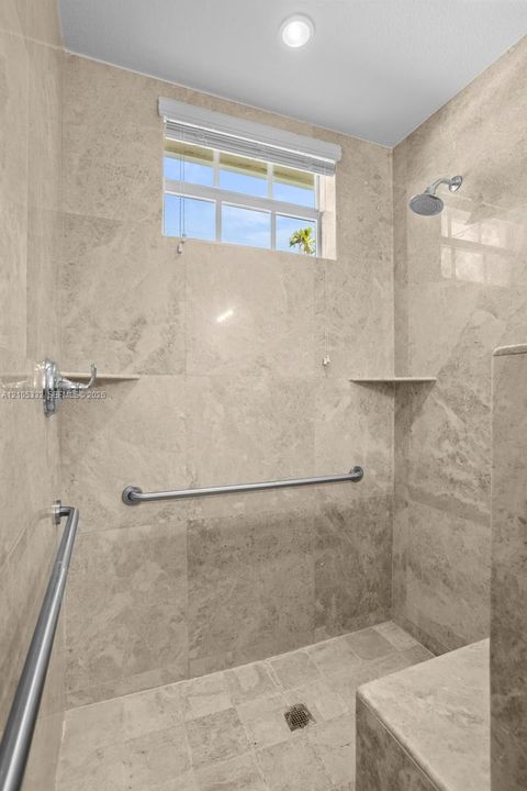 Shower with full-height stone-finish wall tiling, integrated bench, and metal grab bars