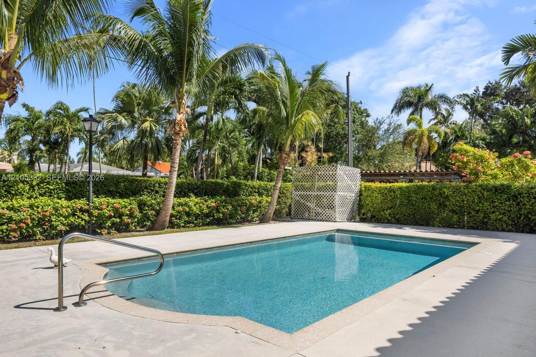 Rectangular swimming pool with integrated steps, surrounded by concrete decking and mature landscaping