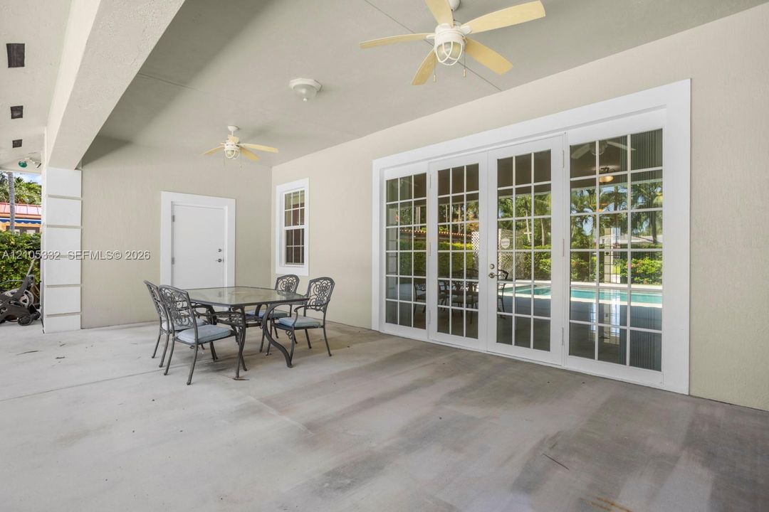 Spacious covered patio with concrete flooring, multiple ceiling fans, and large French doors