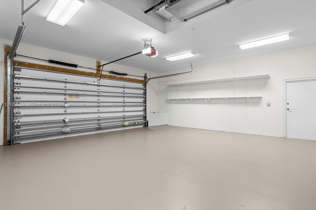 Garage space featuring a roll-up door, built-in shelving, a side access door, and overhead lighting