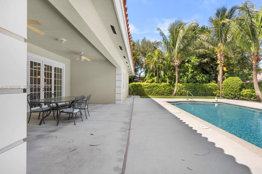 Covered patio with dual ceiling fans, French doors, and an outdoor swimming pool with surrounding hardscaping