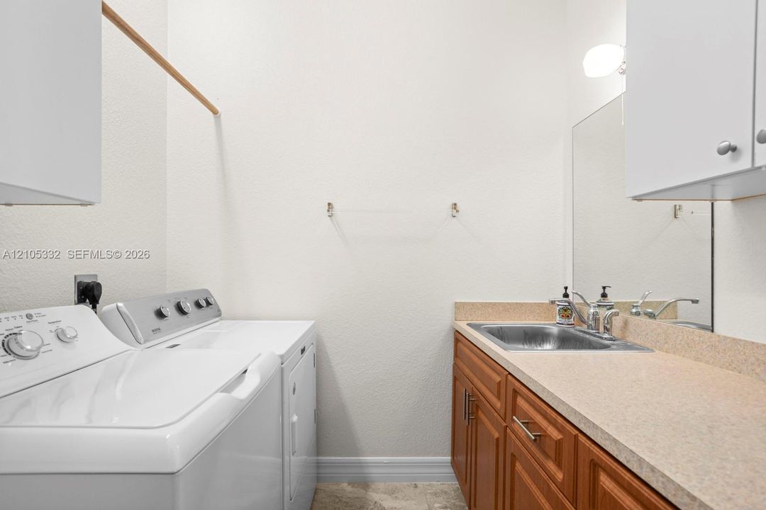 Laundry area with light-toned countertop, wood-finish cabinetry, and a stainless steel utility sink