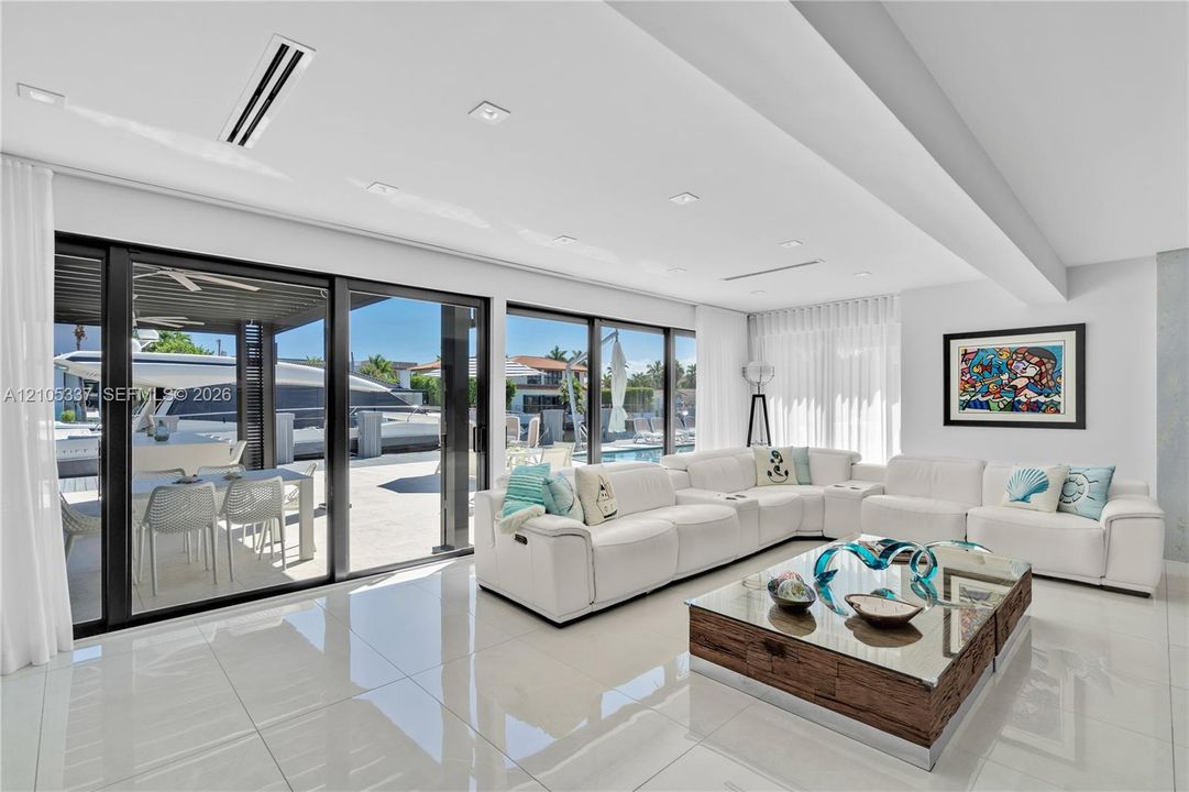 Large-format porcelain tile flooring, recessed ceiling lighting, and expansive floor-to-ceiling sliding glass doors opening to a covered outdoor patio