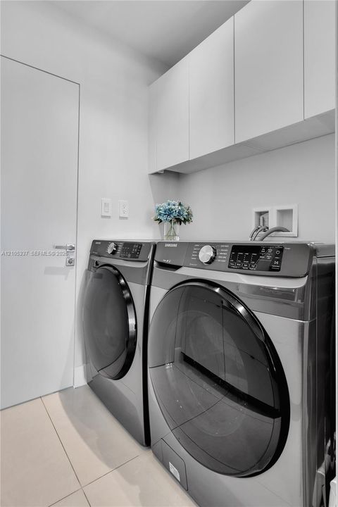 Laundry area featuring flat-panel upper cabinetry, neutral large-format tile flooring, and a sleek solid-core door with modern brushed-metal hardware