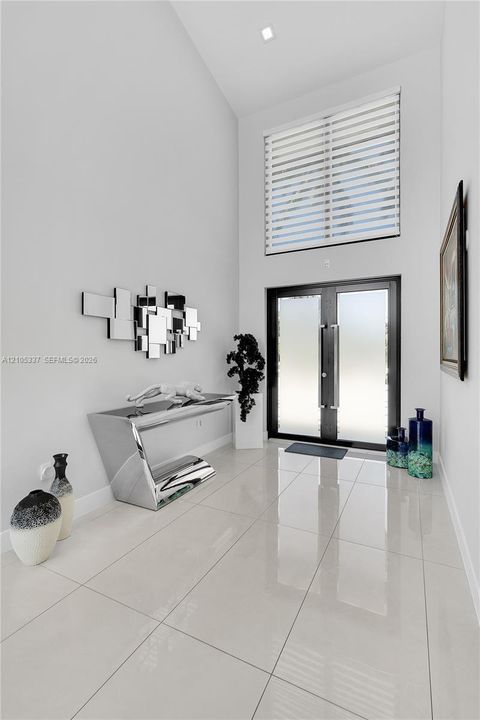 Foyer featuring double entry doors with frosted glass, high ceilings, large-format polished tile flooring, and a transom window