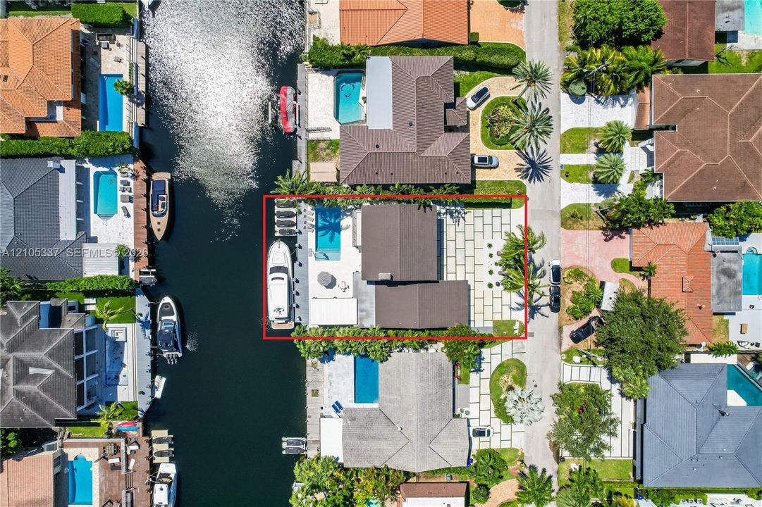 Waterfront property featuring a private boat dock, in-ground swimming pool, expansive stone paver patio, and mature palm trees