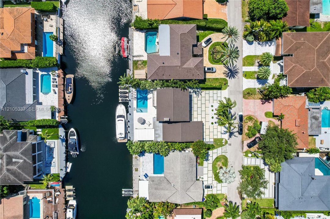 Aerial perspective of a waterfront property featuring a private boat dock, a swimming pool, and a paved stone driveway