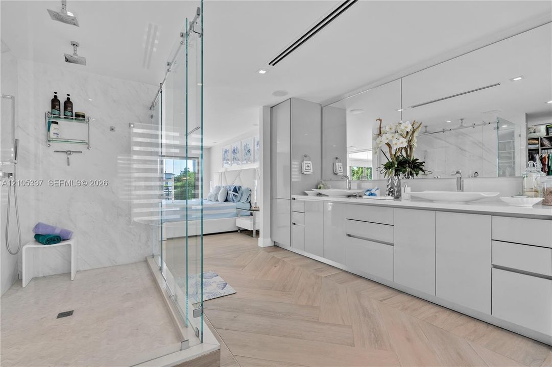 Herringbone wood-finish flooring, glass-enclosed walk-in shower with dual rainfall showerheads, high-gloss dual vanity cabinetry, and large-format wall-mounted mirror