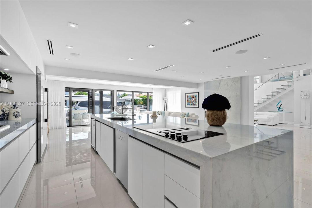 Gourmet kitchen featuring a waterfall-edge center island, solid-surface countertops, flat-panel cabinetry, integrated appliances, and recessed ceiling lighting