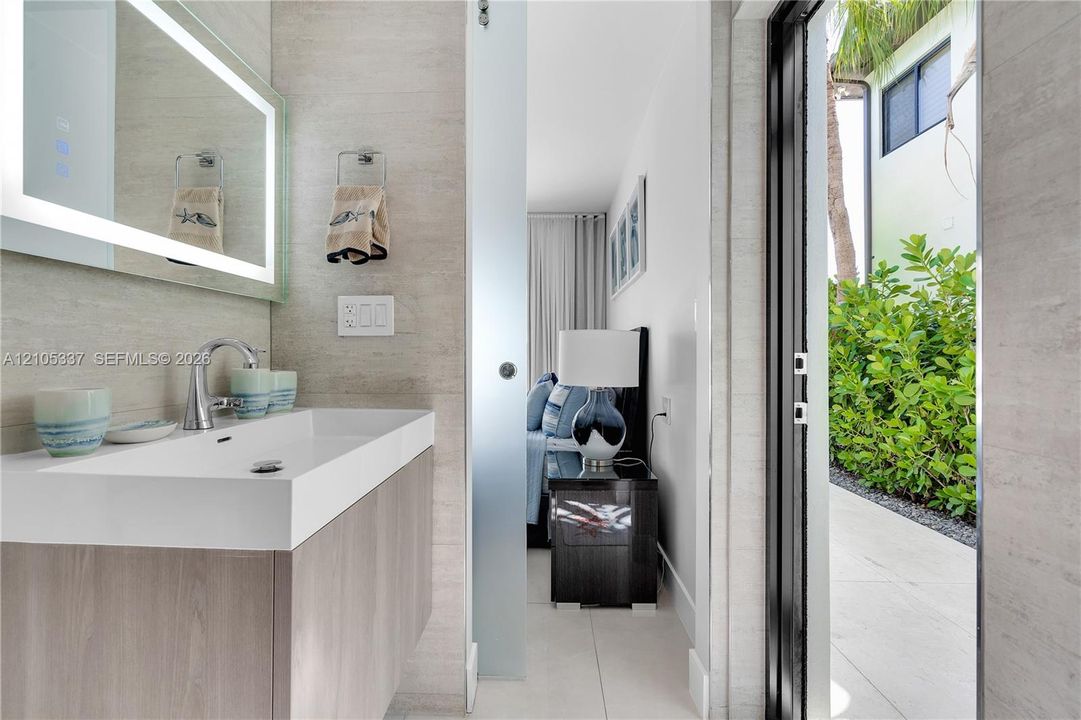 Modern floating vanity with a rectangular integrated sink, LED-backlit mirror, frosted glass sliding door, and stone-finish wall tile