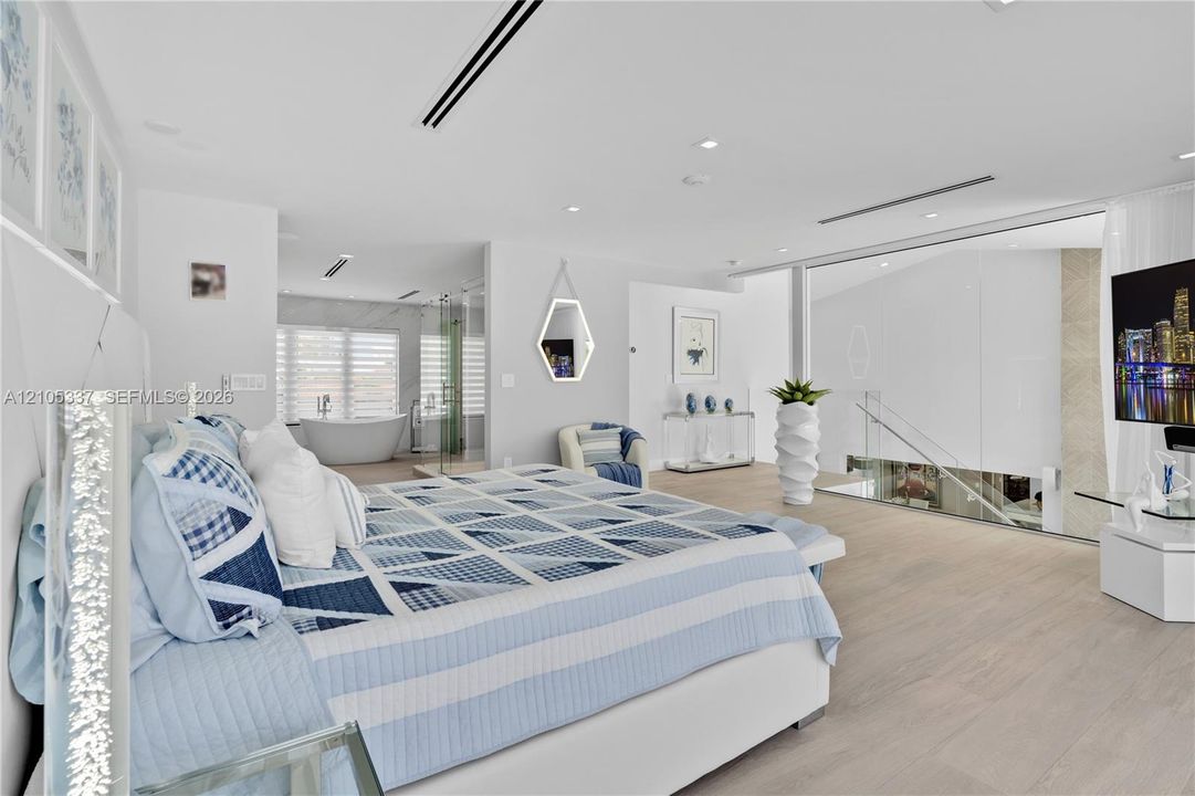 Light-toned wood-finish flooring, recessed lighting, glass partition wall, and soaking tub with neutral stone-style tile