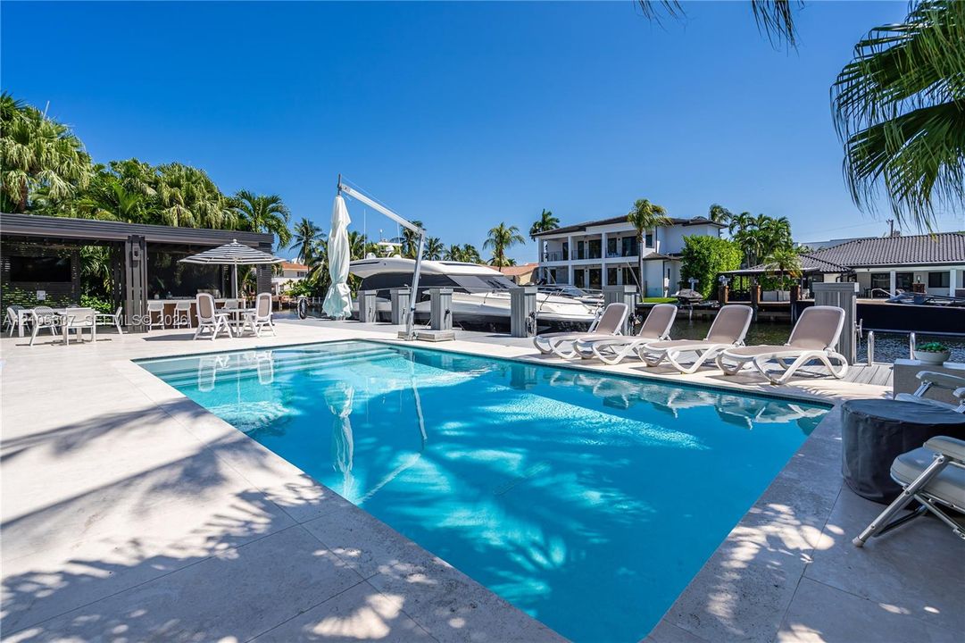 In-ground swimming pool with stone-tile decking, covered outdoor bar area, private boat dock with integrated lift, and seawall bulkhead