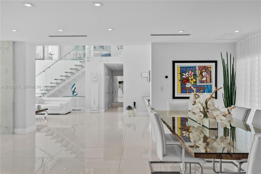 Open-concept interior featuring large-format polished tile flooring, recessed ceiling lighting, and a staircase with glass railings and metal hardware