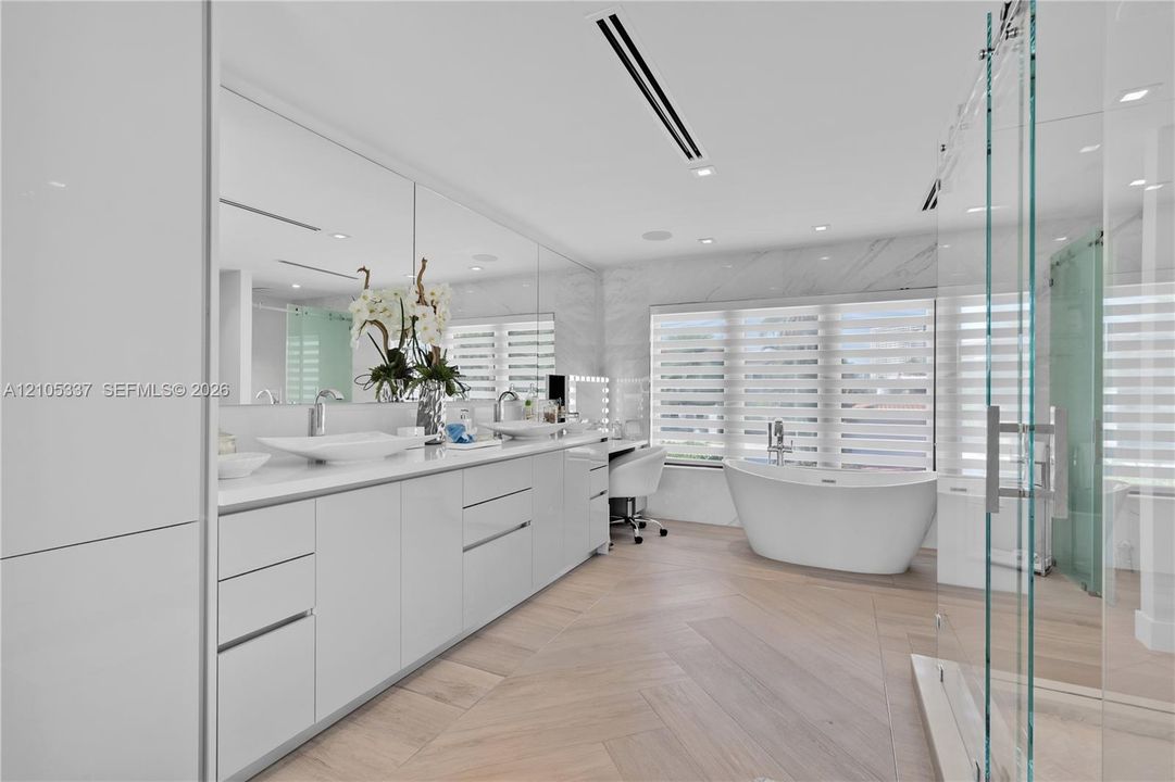 Dual vanity featuring vessel sinks, stone-surface countertop, floor-to-ceiling mirror, freestanding soaking tub, and herringbone wood-finish flooring