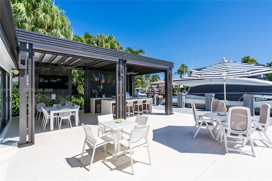 Outdoor patio featuring a covered pergola, built-in kitchen station with bar seating, large-format tile flooring, and direct water access