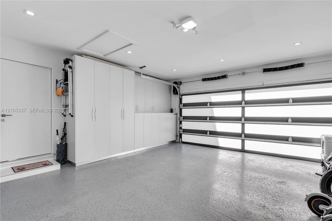 Garage featuring a sectional door with frosted glass panels, built-in floor-to-ceiling cabinetry, recessed lighting, and speckled epoxy flooring