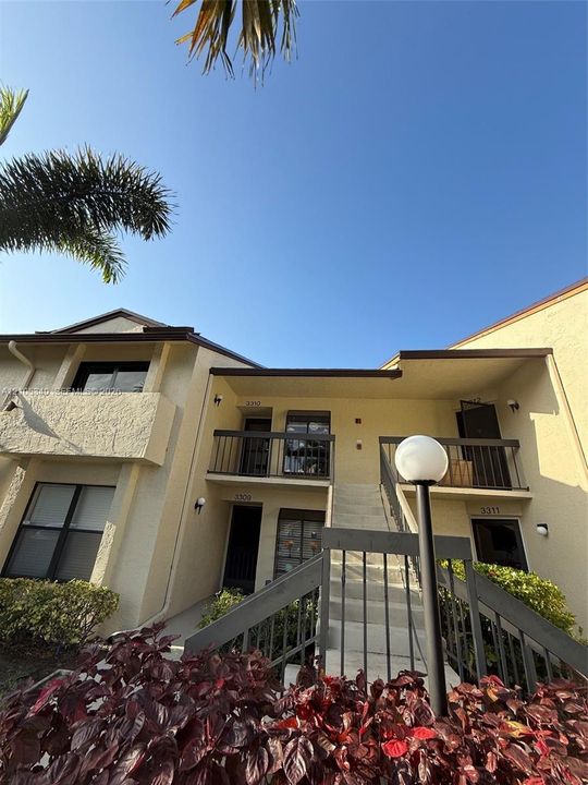 Multi-level building exterior featuring stucco finish, multiple balconies with dark railings, exterior lighting fixtures, and a prominent staircase
