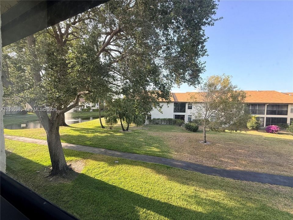 Landscaped grounds featuring a water body with a fountain, mature trees, and a paved pathway