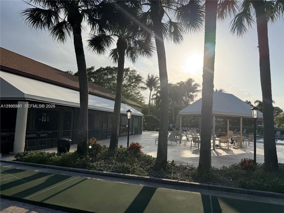 Outdoor shuffleboard court, expansive patio, covered outdoor seating area, mature palm trees, and a building with a shingle roof