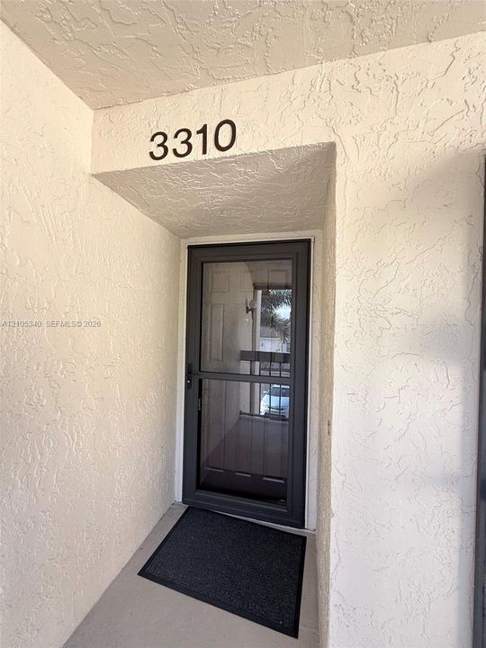Entryway featuring a security door, textured stucco walls, and clear numerical address