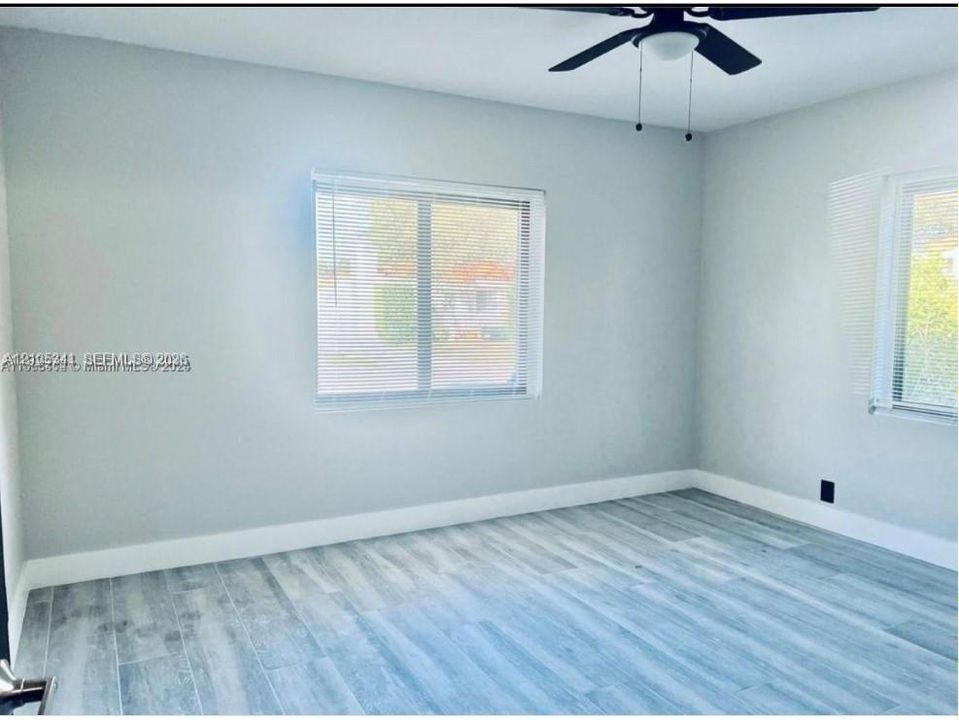 Neutral interior featuring wood-finish flooring, two windows with horizontal blinds, and a ceiling-mounted light fixture with fan