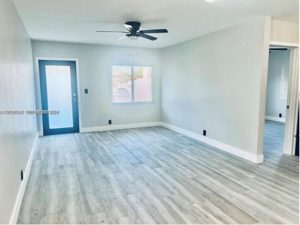 Light-toned wood-finish flooring, white walls, black ceiling fan, and a door with frosted glass panel