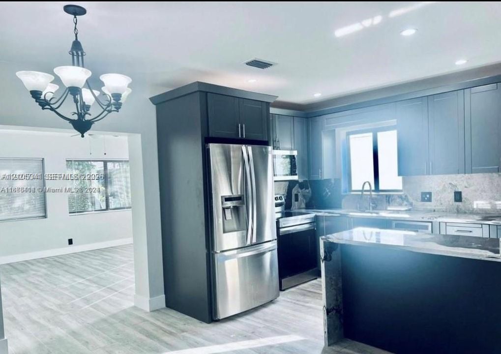 Kitchen featuring charcoal-toned cabinetry, stainless steel appliances, stone-finish countertops, recessed lighting, and a multi-arm chandelier