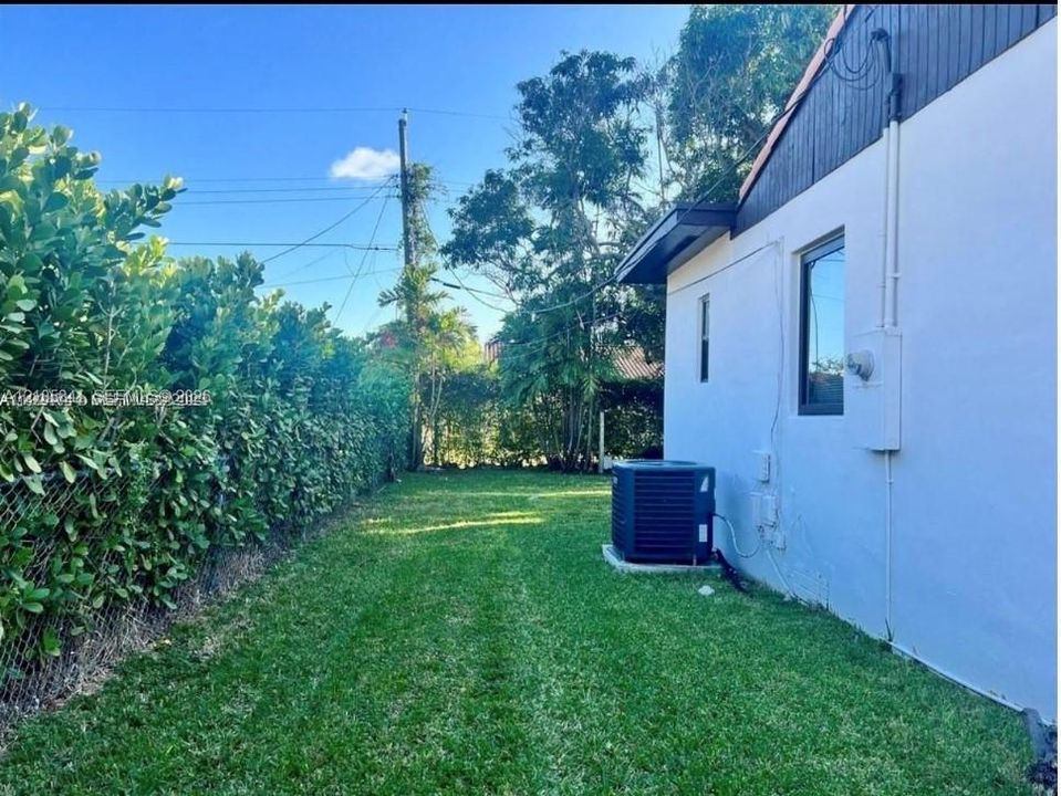 Exterior side yard featuring a manicured lawn, dense perimeter landscaping, and a chain-link fence