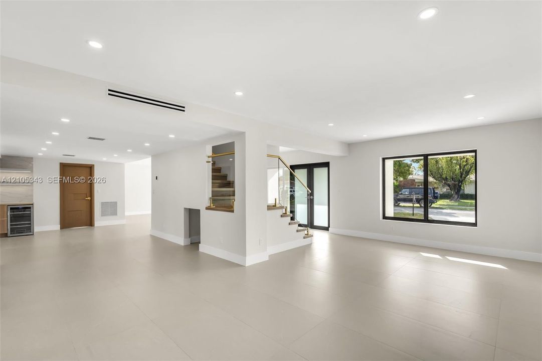 Large-format tile flooring, recessed ceiling lighting, staircase with glass railing, and black-framed exterior doors