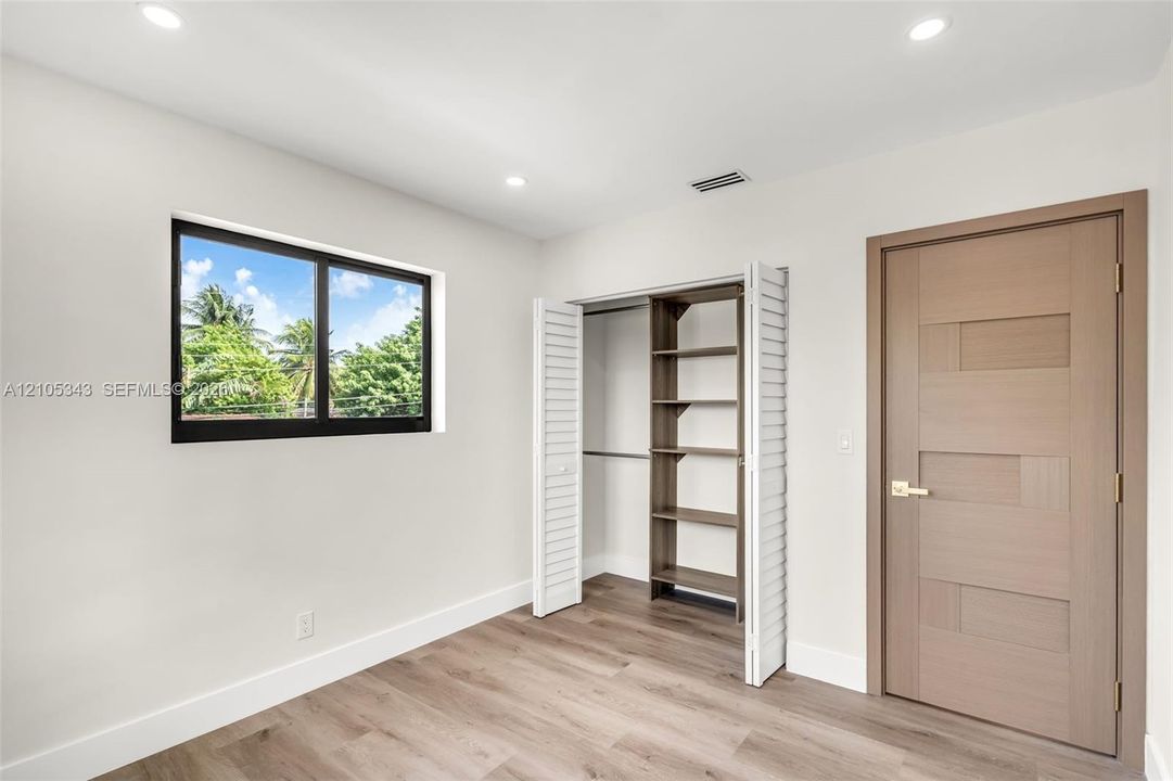 Interior space featuring wood-finish flooring, recessed lighting, a single-pane window with black framing, a closet with built-in shelving, and a wood-textured door with gold-toned hardware