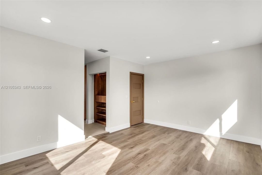 Neutral-toned walls, wood-finish flooring, recessed lighting, and a walk-in closet with built-in shelving