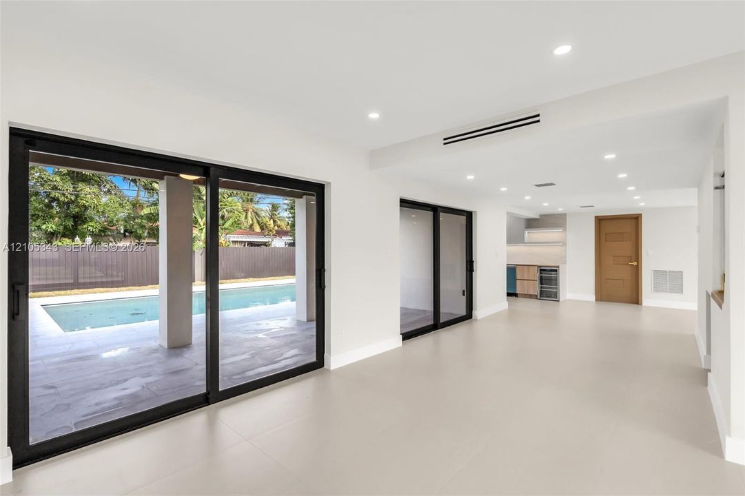 Large-format sliding glass doors with black frames, recessed ceiling lighting, light-toned tile flooring, and integrated kitchenette cabinetry