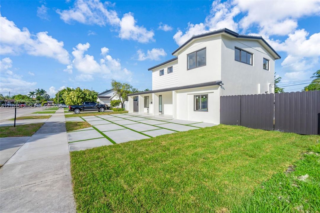 Two-story residence featuring a smooth stucco exterior, multi-panel concrete paver driveway with turf insets, and dark-finished metal privacy fencing
