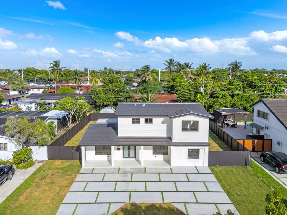 Two-story exterior featuring white horizontal siding, a dark-toned roof, a covered front porch, and a paved grid-pattern driveway with integrated turf strips, all enclosed by dark perimeter fencing