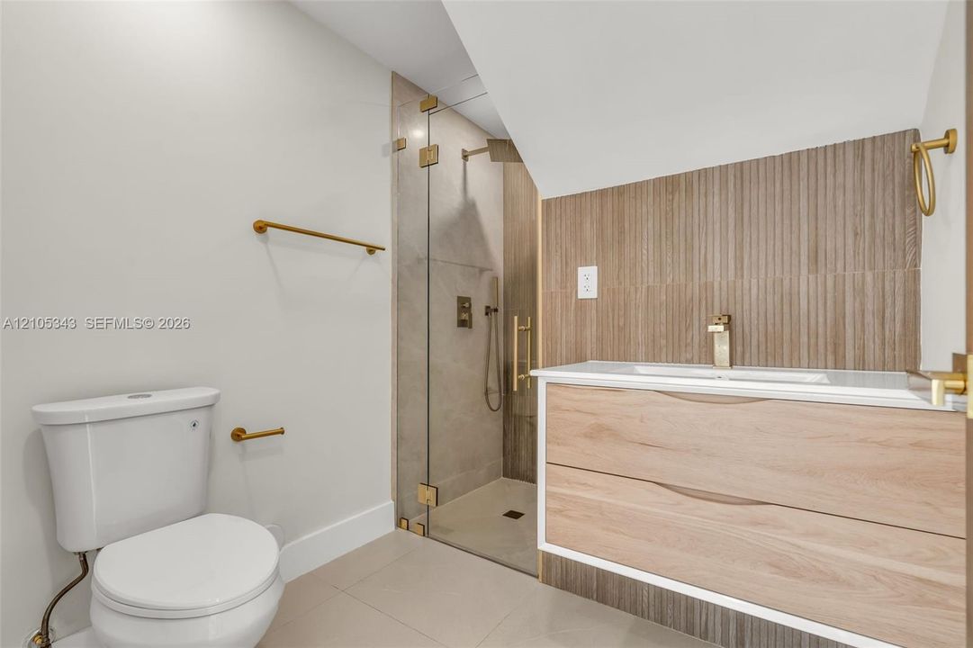 Floating wood-finish vanity with integrated sink, brass-tone hardware, vertical ribbed tile backsplash, and walk-in shower with glass enclosure