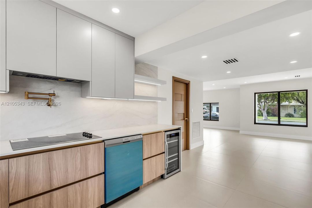 Kitchen featuring custom flat-panel cabinetry, light-toned stone-finish backsplash, built-in beverage refrigerator, wall-mounted pot filler, and recessed lighting
