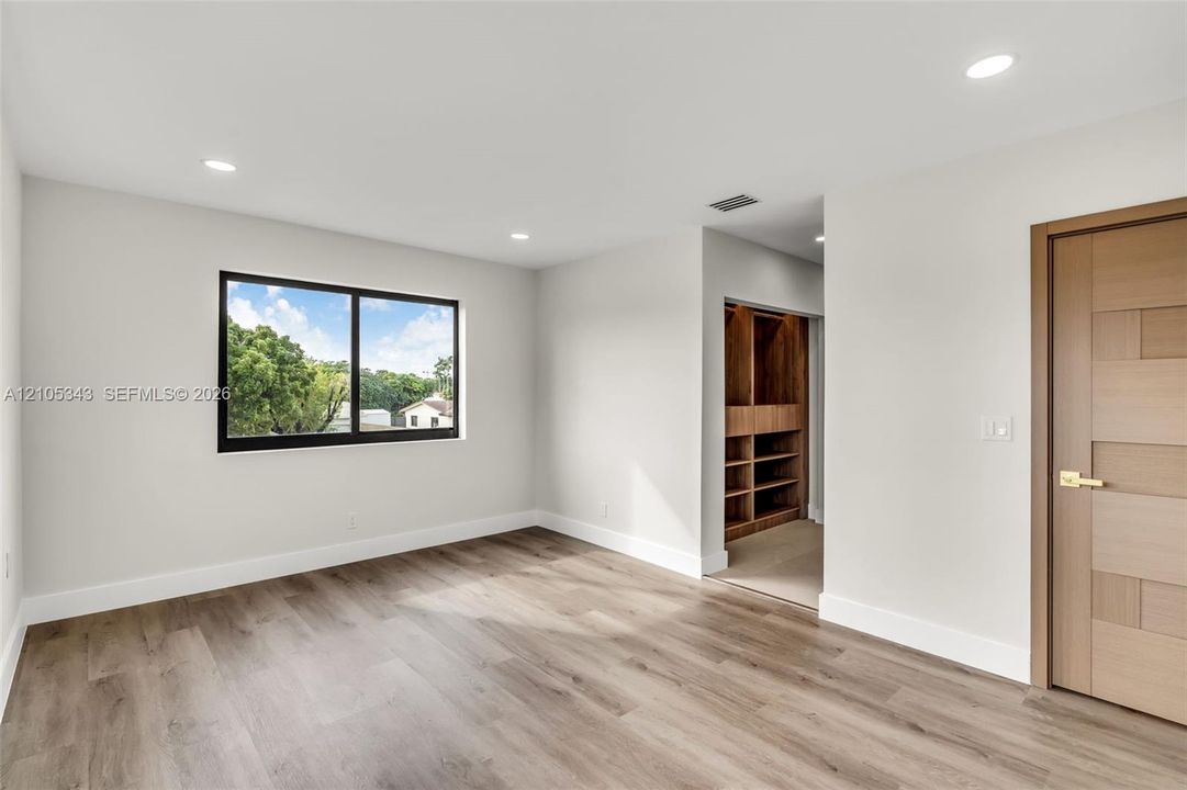 Room featuring wood-finish flooring, recessed lighting, a horizontal sliding window with a dark frame, and a wood-finished door with metallic hardware, complemented by a built-in wooden closet system