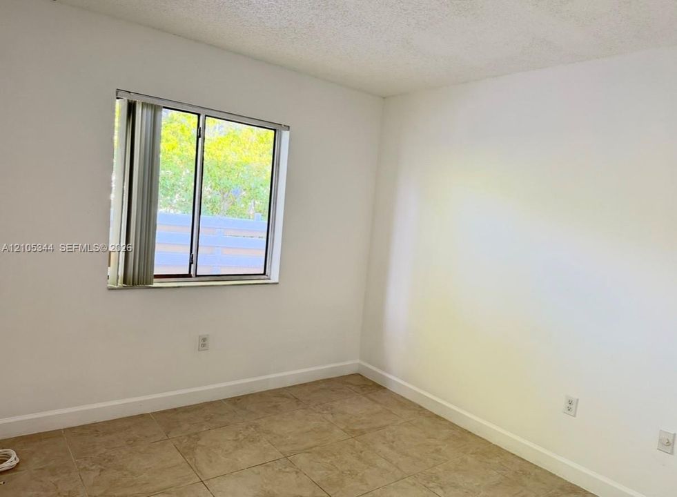 Neutral-toned tiled flooring, white painted walls, and a window with vertical blinds