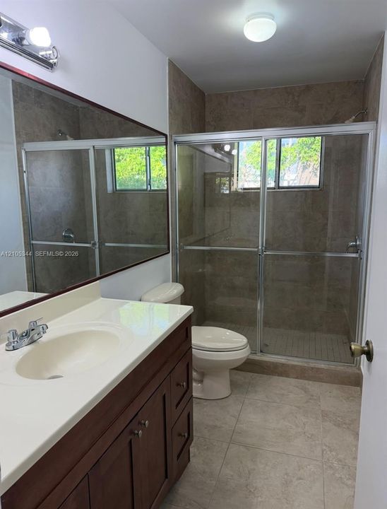 Bathroom featuring a wood-finish vanity with an integrated sink, a glass-enclosed shower, full-height tile shower surround, and tile flooring