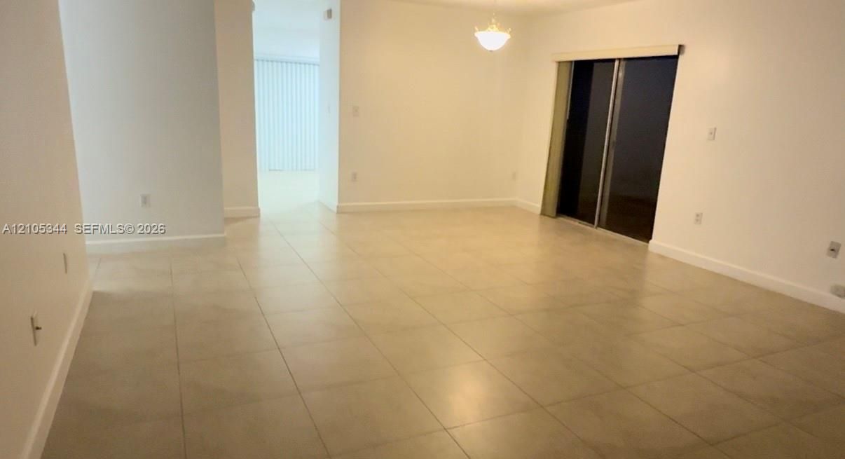 Light-colored tile flooring, overhead lighting, sliding glass door, white wall finishes, and a hallway