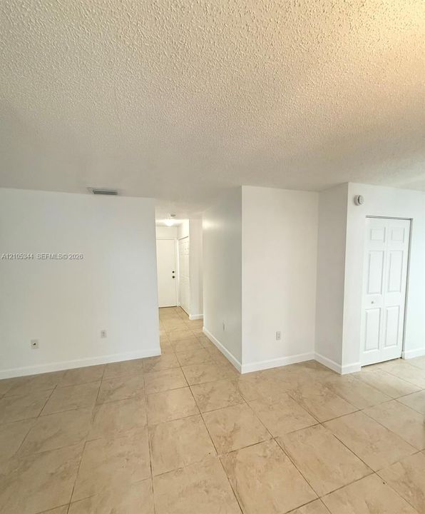 Neutral tone tiled flooring, white walls, and a textured ceiling