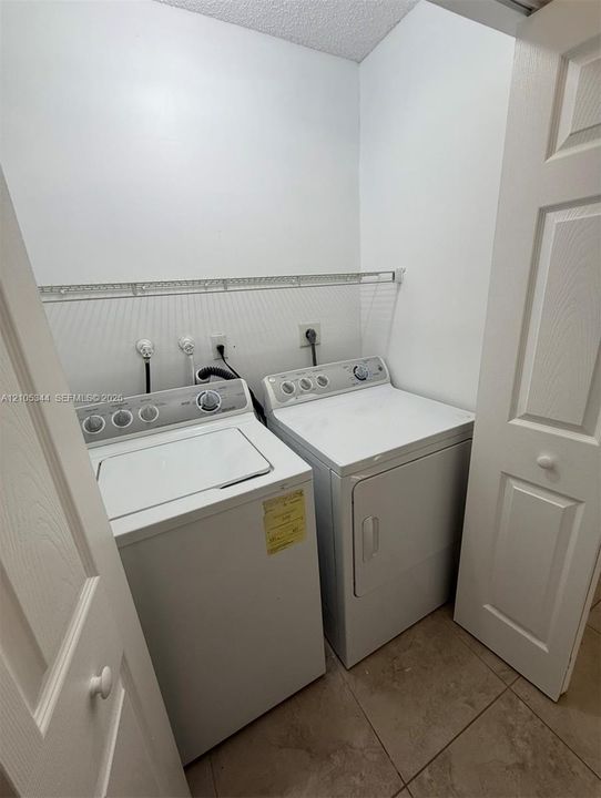 White washer and dryer units, tile flooring, and a wire storage shelf