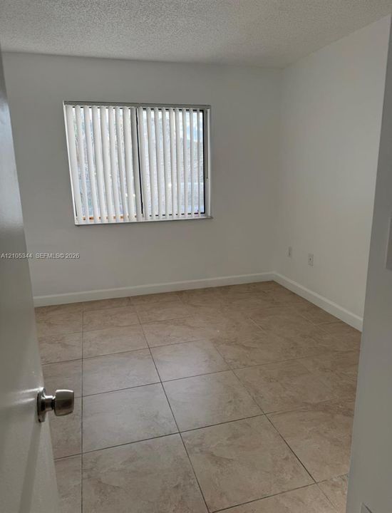 Neutral-toned tile flooring, window with vertical blinds, and white painted walls