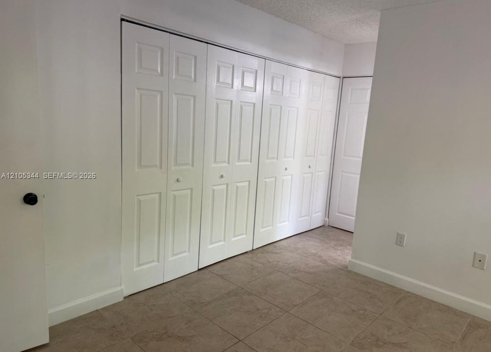 Neutral-toned tile flooring, white walls, and white bi-fold closet doors
